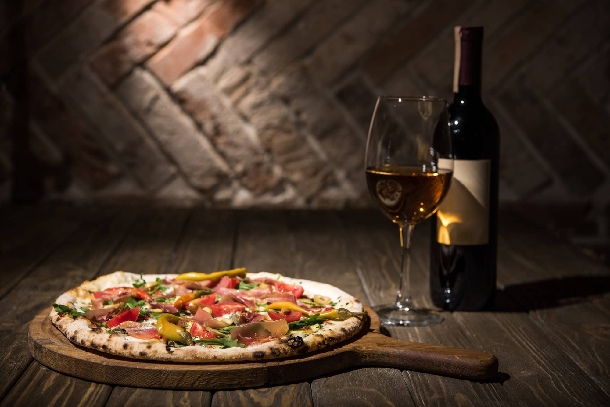 selective focus of italian pizza, bottle and glass of wine on wooden tabletop